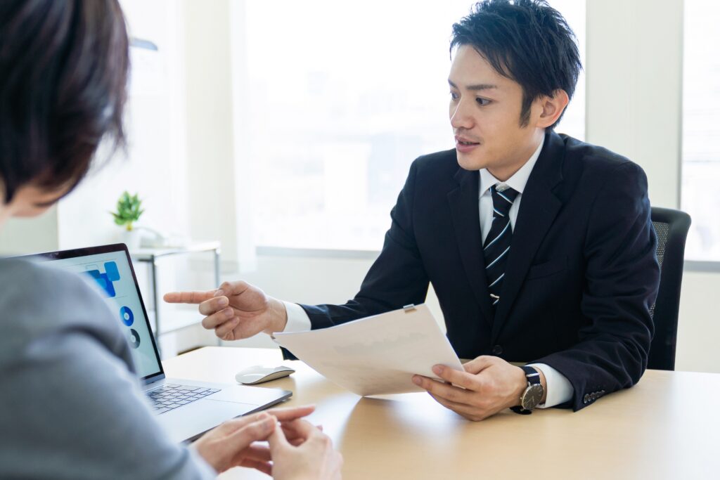 スーツ着用の男性がタブレットと資料を女性に見せながら説明している