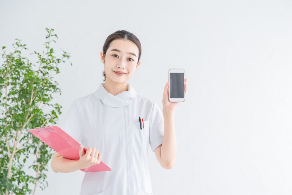 白衣を着た女性がカルテとスマホを持っている